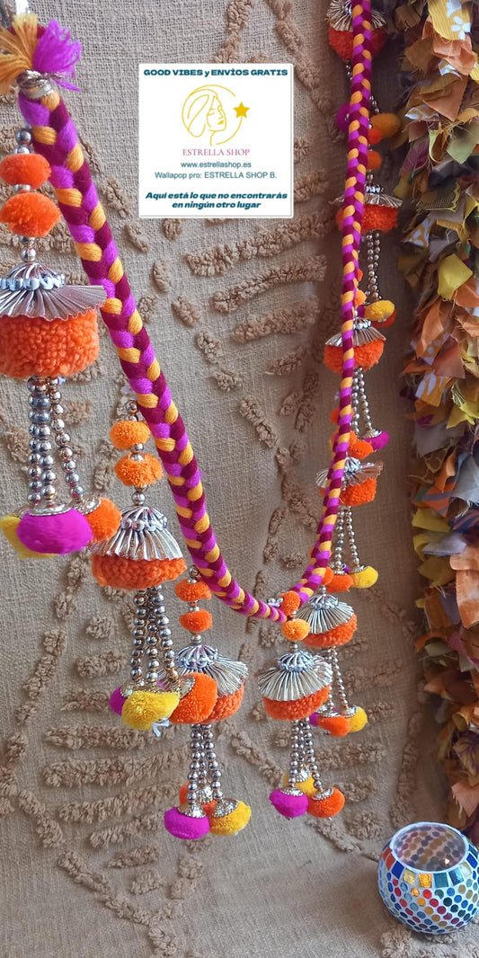 Una pieza original que llena de vida cualquier espacio gracias a su diseño vibrante y lleno de detalles. Esta guirnalda artesanal combina hilos trenzados con pequeñas decoraciones textiles y metálicas que crean un efecto visual alegre y lleno de movimiento. Un elemento exclusivo que transmite la esencia del estilo boho y la riqueza de la artesanía tradicional.