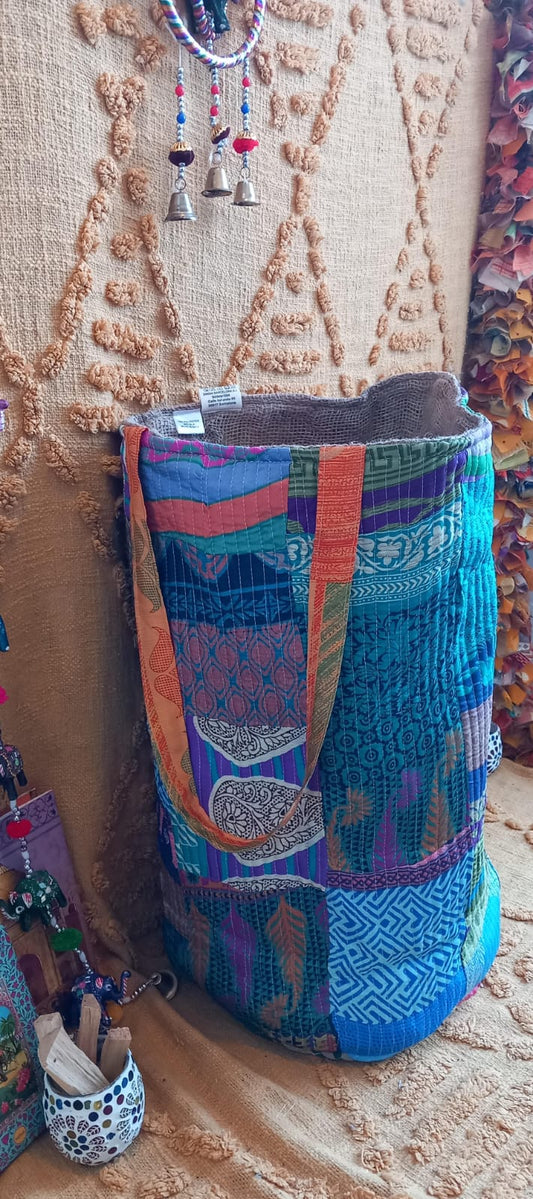 El Cesto Wild Saree 35x50 cm es una pieza artesanal multifuncional que destaca por su exclusividad, sostenibilidad y versatilidad. Confeccionado con telas sedadas recicladas de saree y yute, cada cesto es único gracias a sus vibrantes colores y estampados elaborados con la técnica de patchwork. Su diseño práctico y amplio permite utilizarlo como bolso, elemento decorativo o almacenamiento para el hogar, aportando un toque auténtico de artesanía india a cualquier espacio.