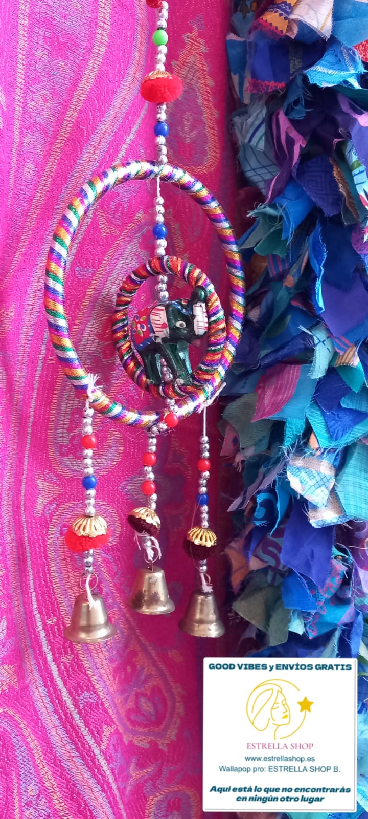 Un colgador encantador que combina tradición y ternura. Este móvil decorativo está elaborado artesanalmente con tela y presenta una estructura circular de la que cuelgan campanas metálicas que producen un suave sonido al moverse con el aire. En su centro, un elefante de la suerte aporta un toque simbólico y alegre. Perfecto para decorar habitaciones infantiles, escaparates o como detalle especial en un rincón de tu hogar. Su estilo suave y colorido lo convierte en un regalo ideal.