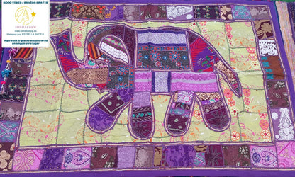 Un clásico del arte textil reinventado con un toque exótico y exclusivo. El tapiz patchwork cuadrado de 150x100 cm está confeccionado artesanalmente con retales bordados en algodón, creando composiciones únicas con flores, formas geométricas y pequeños abalorios brillantes. Cada pieza tiene su propio carácter, con un ribete en tono coordinado que enmarca el diseño y lo convierte en una joya decorativa. Ideal para colgar, usar como camino de mesa o sobre un mueble que quieras destacar.