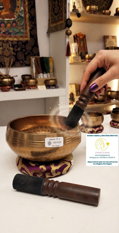 CUENCO GRABADO DE LATÓN GOLPEADO 557G IINCLUYE ZAFU YY STICK DE MADERA.-Un instrumento ancestral con un sonido único y envolvente. El Cuenco de latón pulido es una pieza artesanal elaborada en Nepal, donde cada detalle ha sido cuidadosamente trabajado para ofrecer una vibración profunda y armonizadora. Desde tiempos remotos, estos cuencos han sido utilizados por lamas y sanadores tibetanos para inducir estados de meditación, relajación y bienestar. Su acabado en bronce dorado y sus grabados tradicionales lo