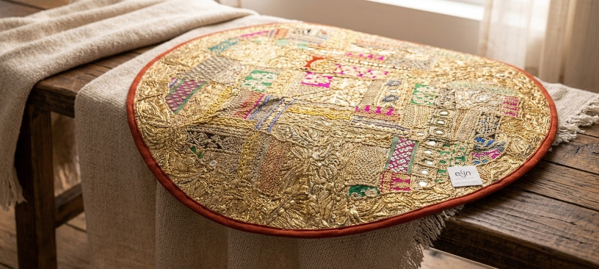 Una pieza que brilla con luz propia y llena de personalidad cualquier espacio. El textil brillante redondo de 90x100 cm aprox. está elaborado artesanalmente a partir de retales decorados con bordados, lentejuelas e hilos metálicos en tonos dorados. Es una unidad diferente, con ribetes únicos y una parte posterior lisa granate para mayor versatilidad. Su tamaño generoso lo convierte en un elemento decorativo central en ambientes bohemios y étnicos.