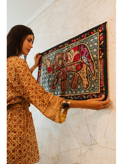 Un clásico del arte textil reinventado con un toque exótico y exclusivo. El tapiz patchwork cuadrado de 90x60 cm está confeccionado artesanalmente con retales bordados en algodón, creando composiciones únicas con flores, formas geométricas y pequeños abalorios brillantes. Cada pieza tiene su propio carácter, con un ribete en tono coordinado que enmarca el diseño y lo convierte en una joya decorativa. Ideal para colgar, usar como camino de mesa o sobre un mueble que quieras destacar.